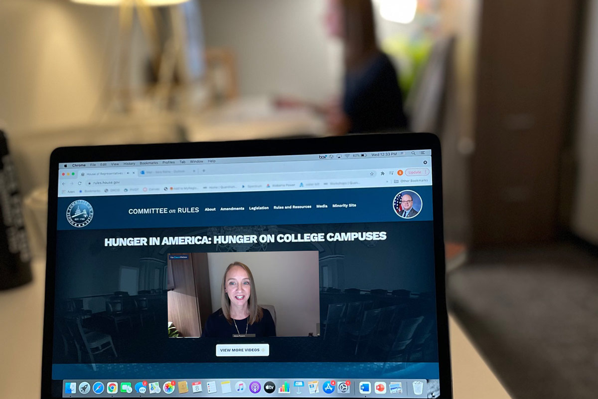 Photo of laptop screen with Powers in the background at her desk.