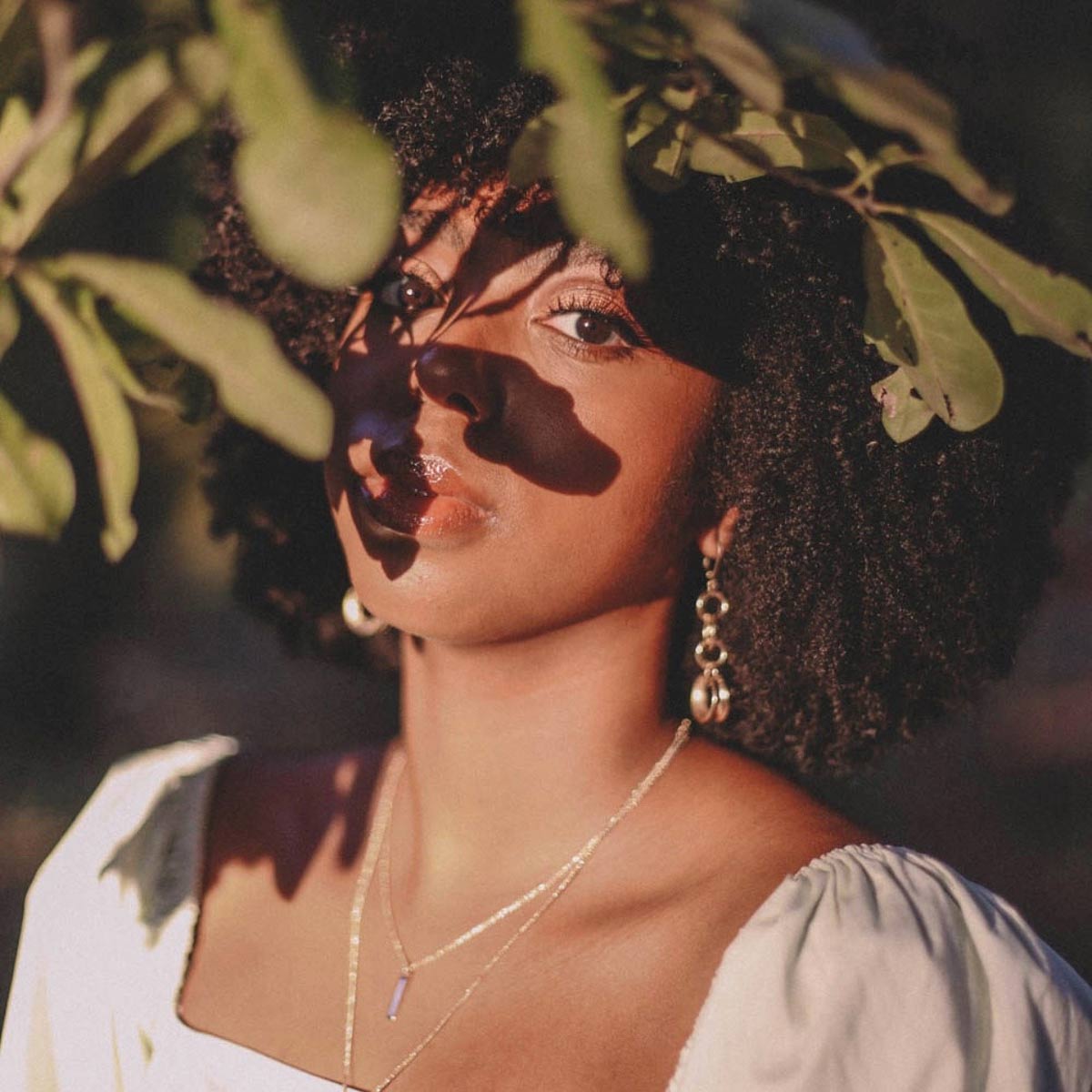 Photo of young lady with tree leaves partially covering her face.